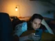 Woman lying on couch at night scrolling on her phone with a tired expression, illustrating doomscrolling and digital fatigue.